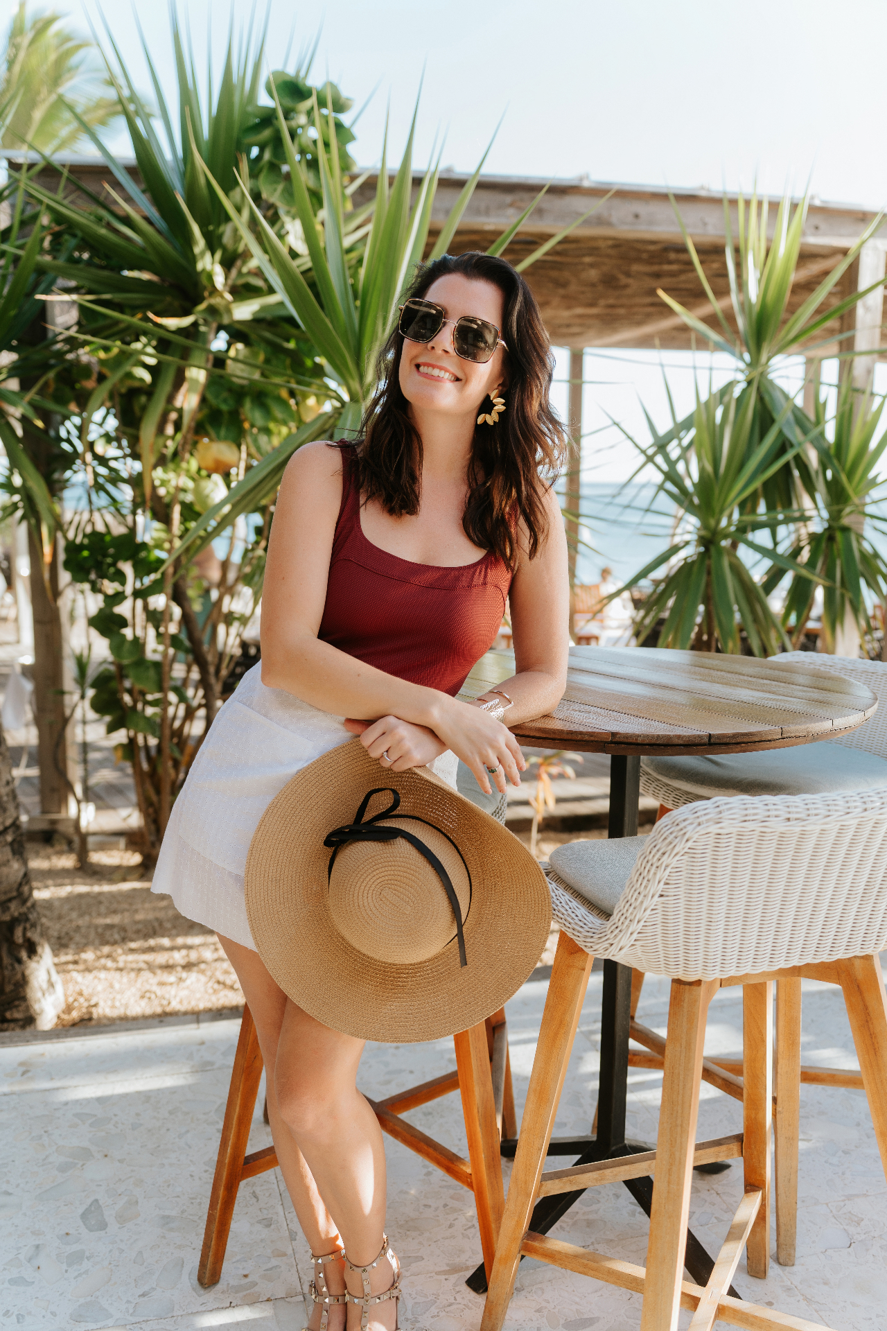 Jennifer Constant outdoors holding a sun hat by a palm tree